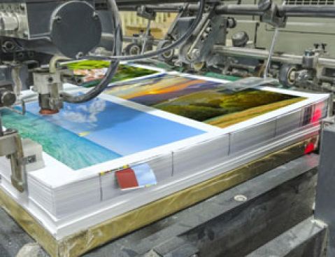 Offset machine printing a stack of posters